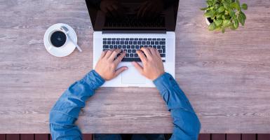 Męskie ręce przy biurku wciskają klawisze laptopa (fotografia)
